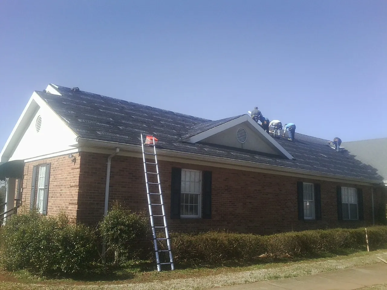 Crew tearing shingles off a brick ranch roof with a ladder set — Emergency Roof Repair work by our crew in Crumpler