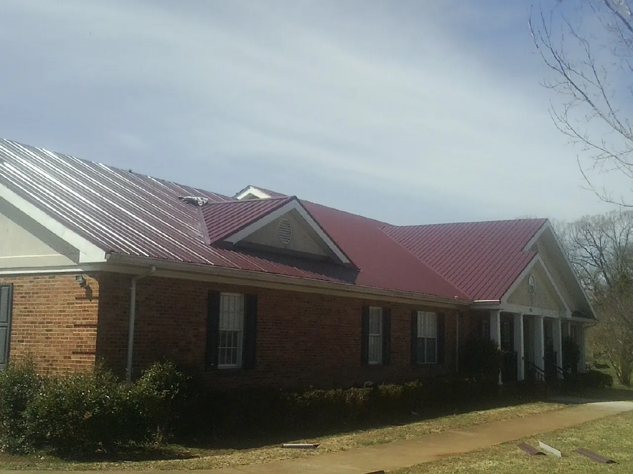 Red metal roof with gabled entries on a long brick building, from a Hail Damage Roof Repair job in Crumpler