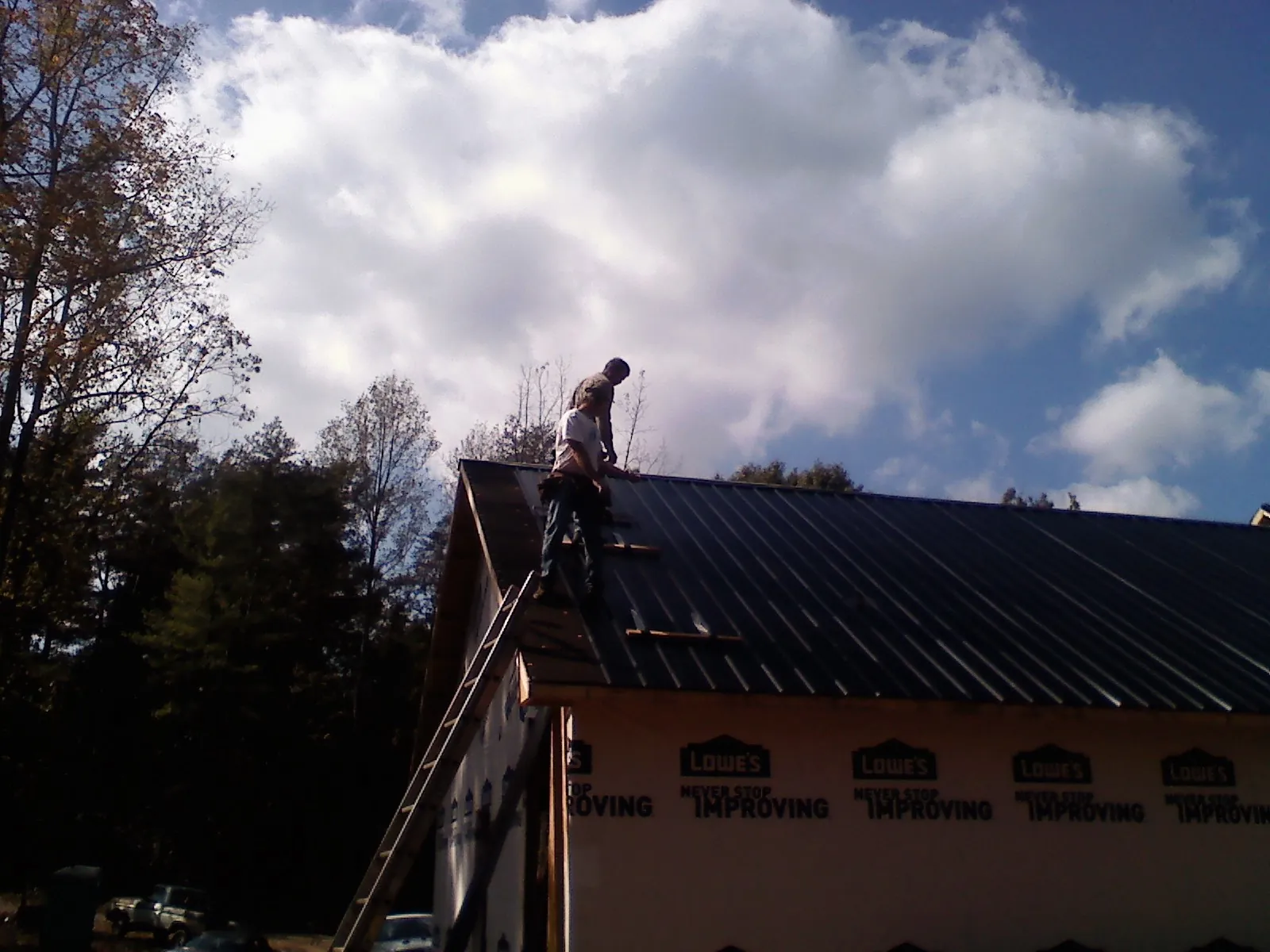 Roofer fastening dark metal panels high against a cloudy sky, from a Roof Inspection job in Crumpler