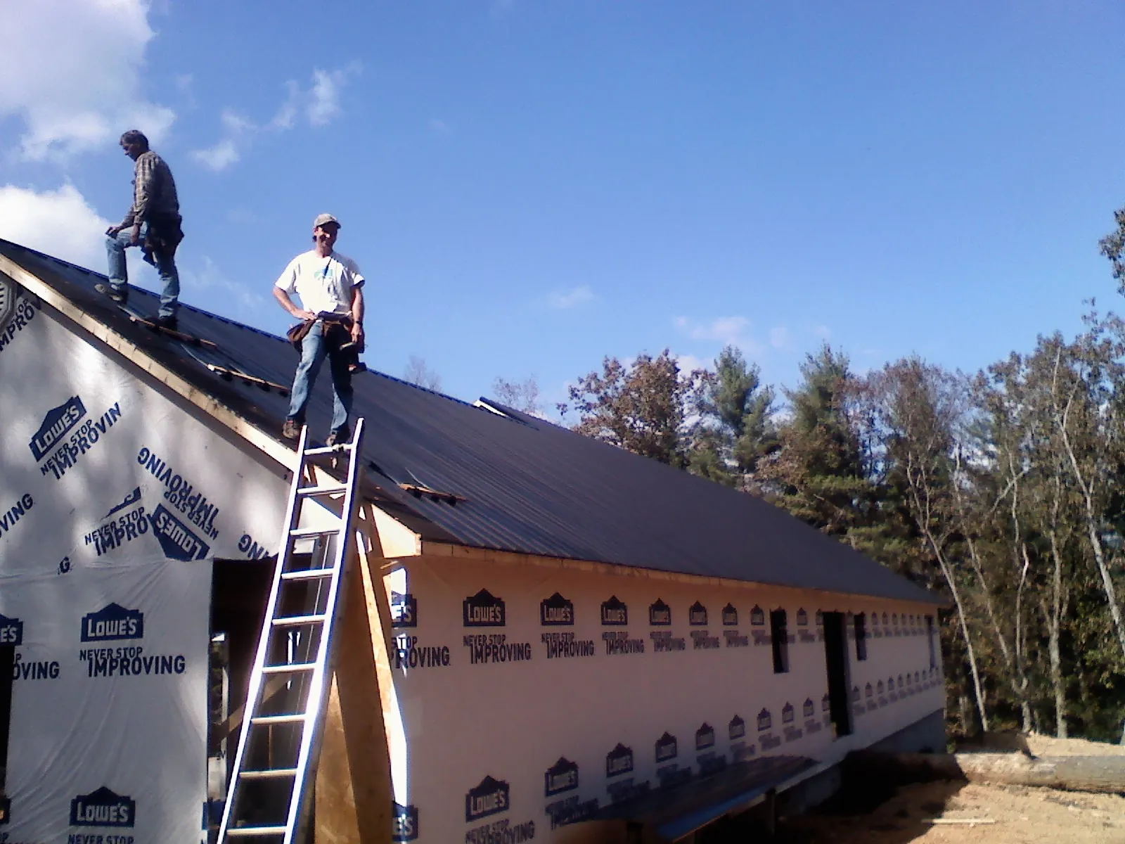 Two roofers standing on a long dark metal roof over a wrapped building in Crumpler