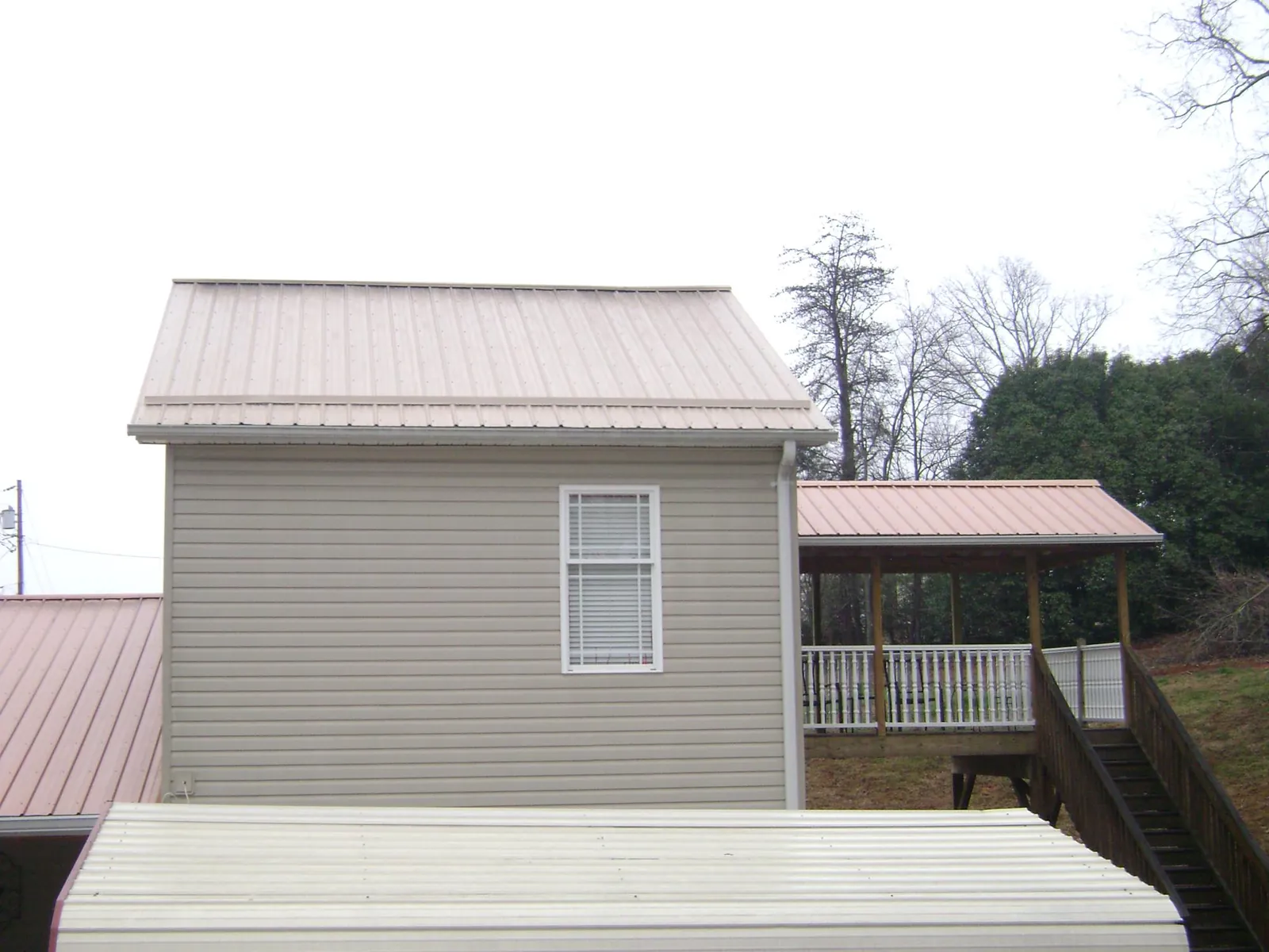 Tan metal roofs on a two story addition and attached porch, from a Roof Replacement job in Crumpler