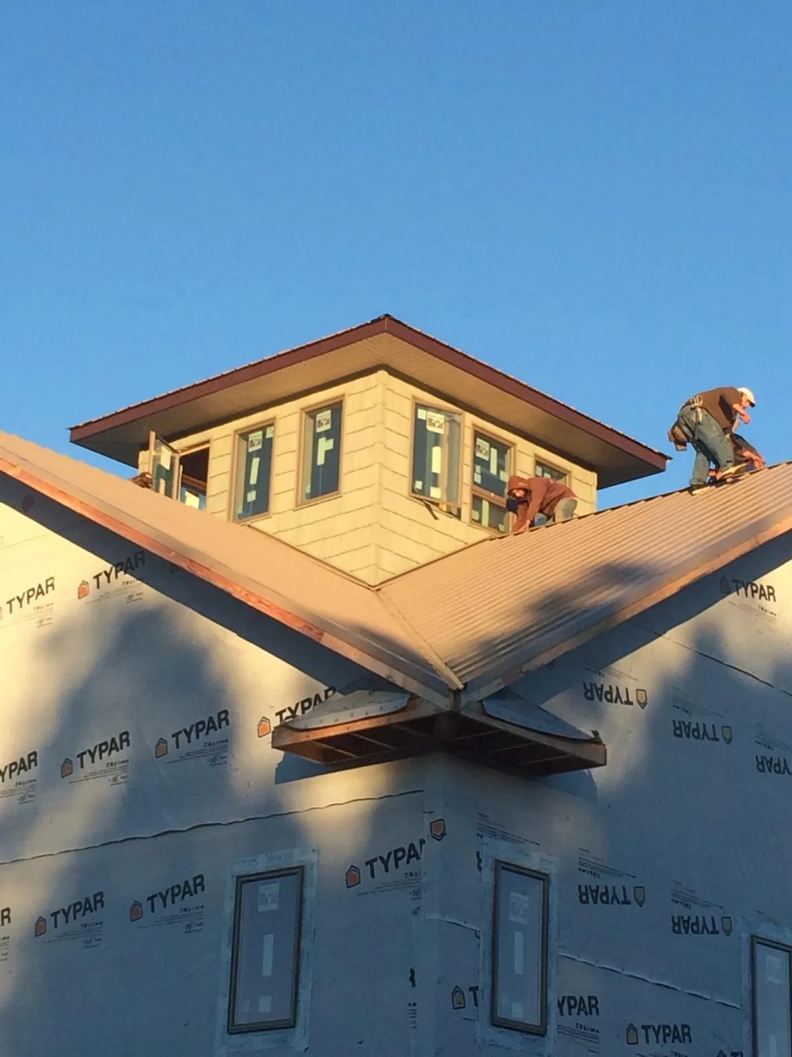 Roofers working around a rooftop cupola on a new metal roof at sunset — Roof Waterproofing in Crumpler by Roofing Brothers